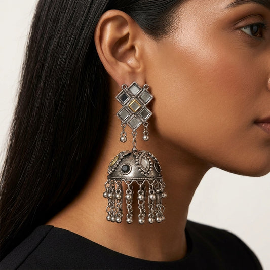 Close-up of geometric jhumka earring worn beside the face, showing ornate dome and dangling chain fringe