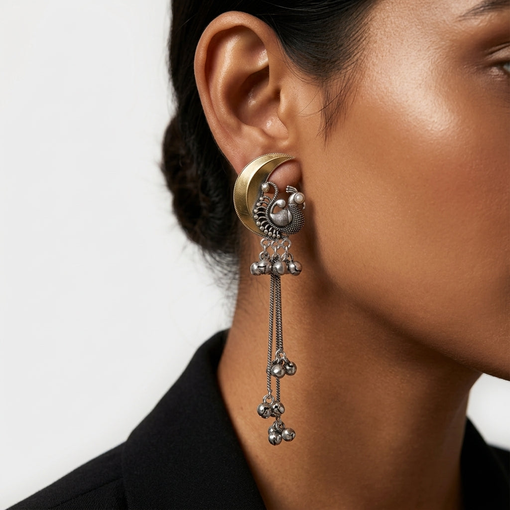 Close-up side view of crescent earrings with ornate details and long dangling chains on an ear