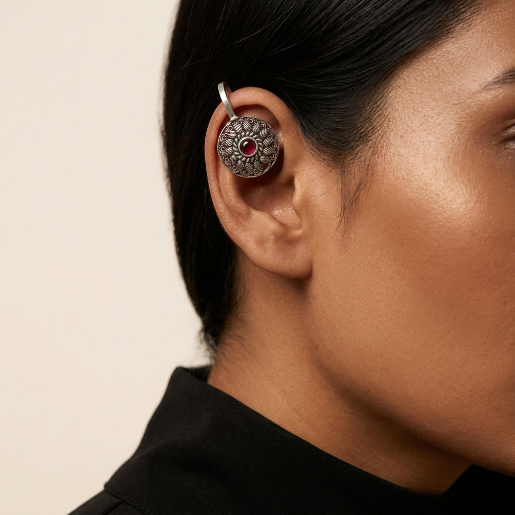 Close-up side view of round patterned earring with red centre worn on upper ear