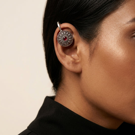 Close-up side view of round patterned earring with red centre worn on upper ear