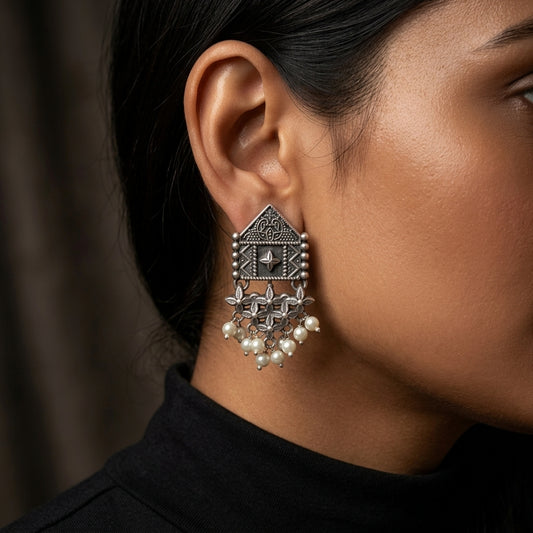 Close-up side view of ornate geometric earring with dangling white beads worn against dark clothing
