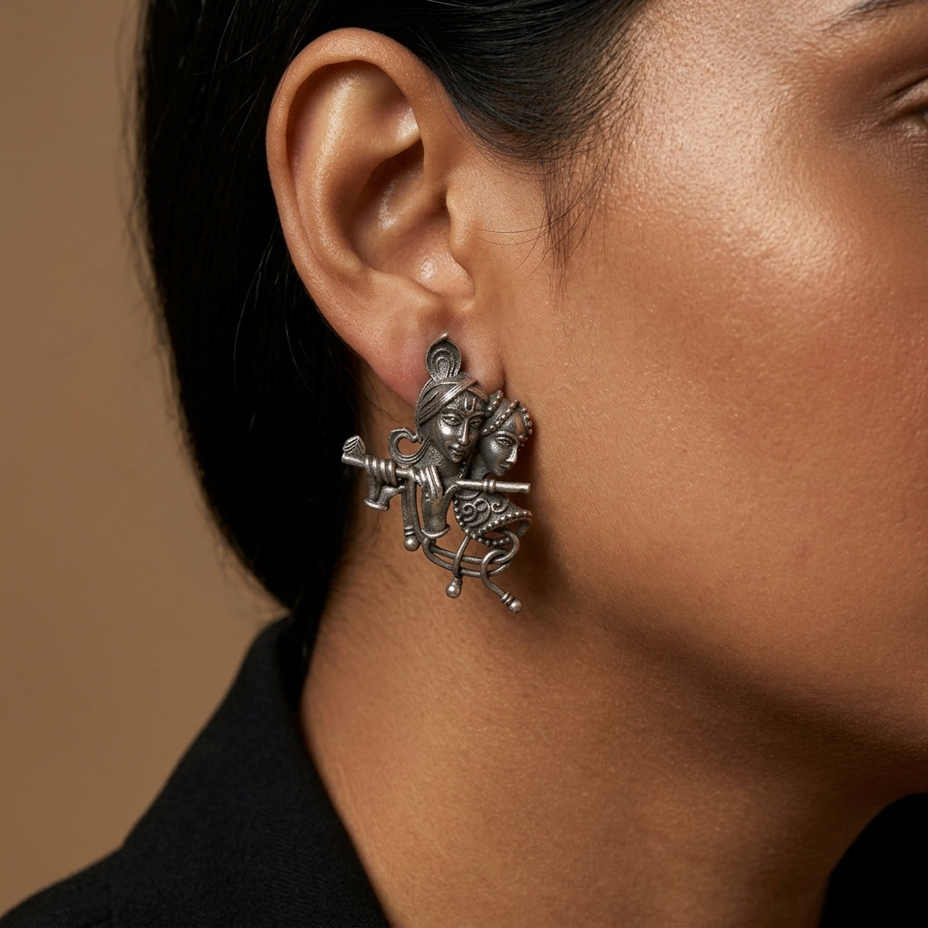 Close-up side view of ornate figurative drop earring worn against cheek, neck, and black clothing.