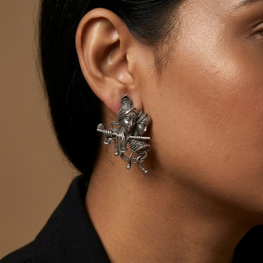 Close-up side view of ornate figurative drop earring worn against cheek, neck, and black clothing.