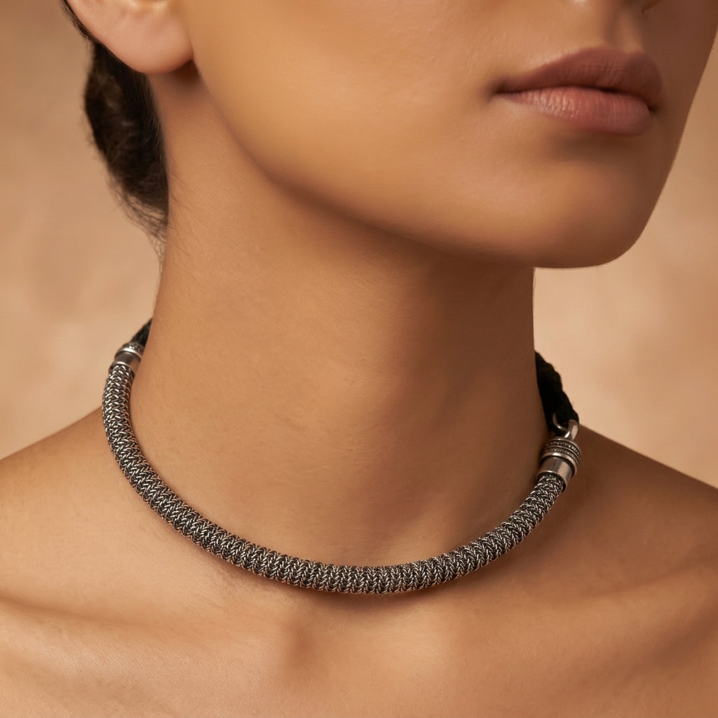 Close-up of a dark silver-toned woven necklace resting around a model’s neck and shoulders