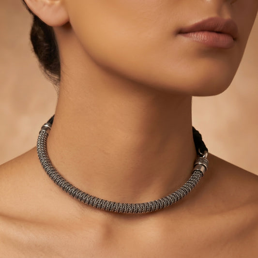 Close-up of a dark silver-toned woven necklace resting around a model’s neck and shoulders
