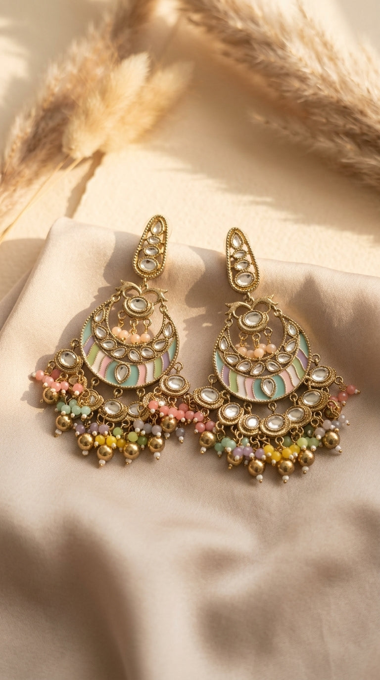 Matching chandbali earrings arranged on pale fabric, showing enamel panels, stones, and multicoloured bead fringe