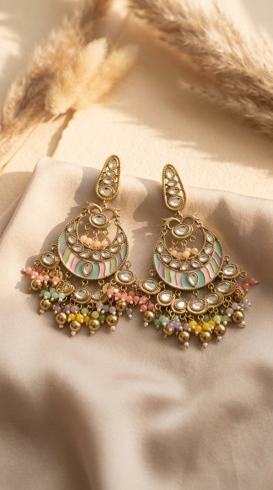 Matching chandbali earrings arranged on pale fabric, showing enamel panels, stones, and multicoloured bead fringe